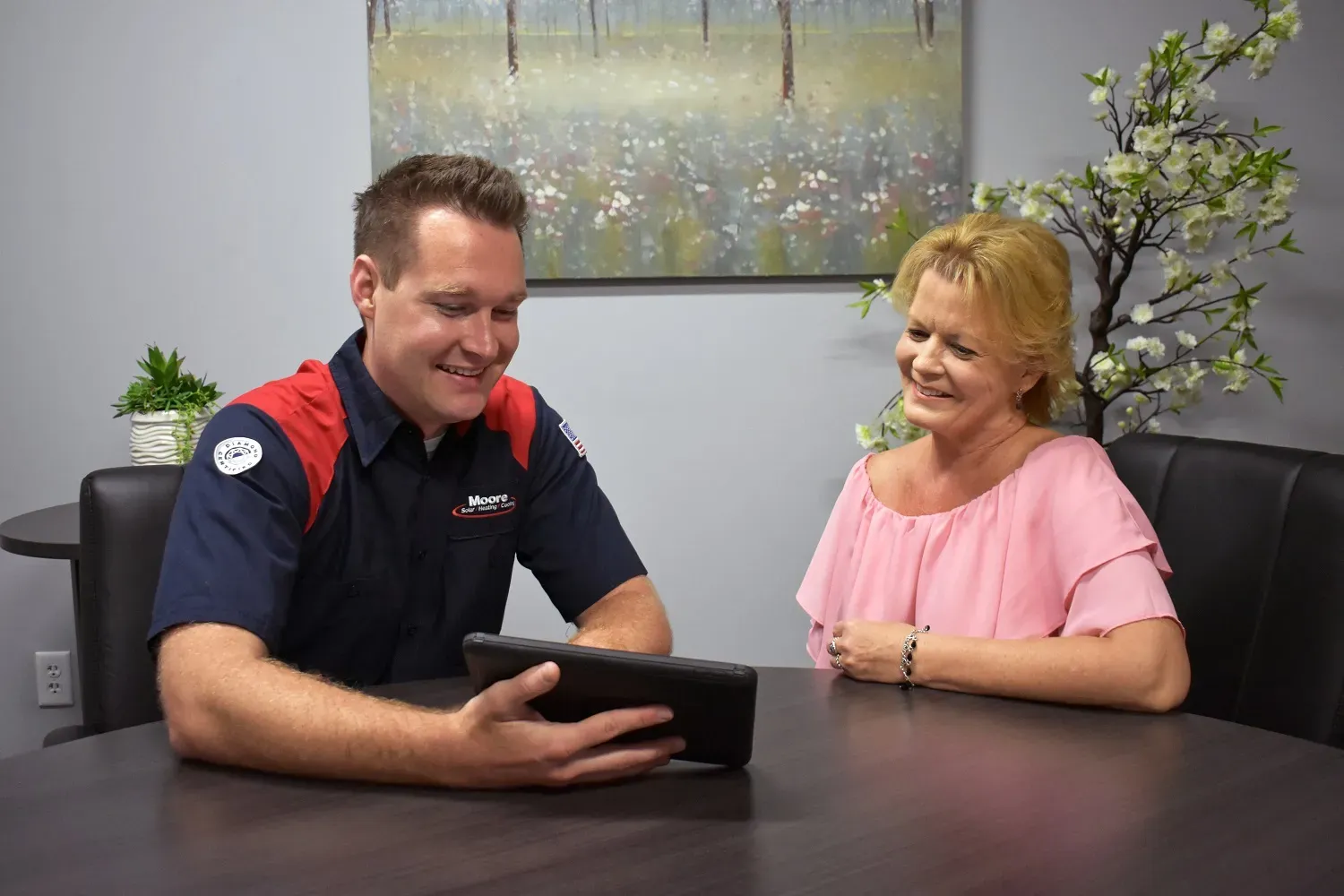 A Moore Home Services professional consults with a smiling woman at a table, using a tablet in an office setting.